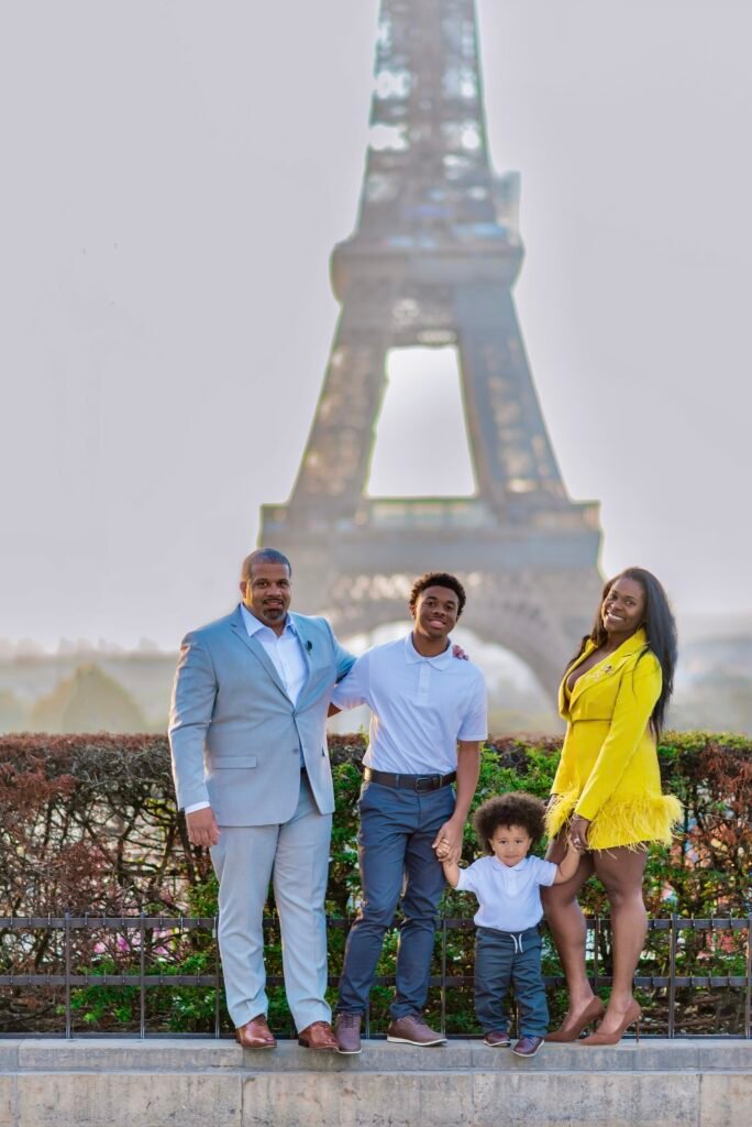 Black family of 4 in Paris France standing with the Eiffel Tower in the background on a cloudy day